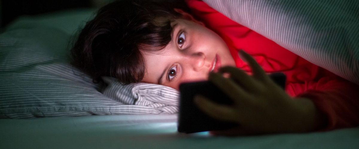 Et barn under dynen med en telefon, der lyser i mørket