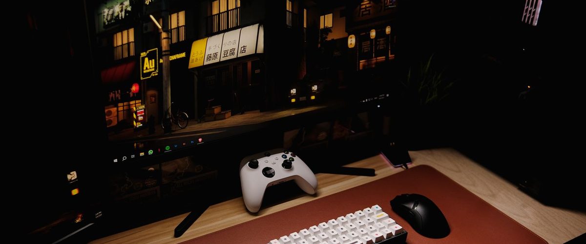 En controller, et tastatur og en skærm i et mørkt værelse om aftenen