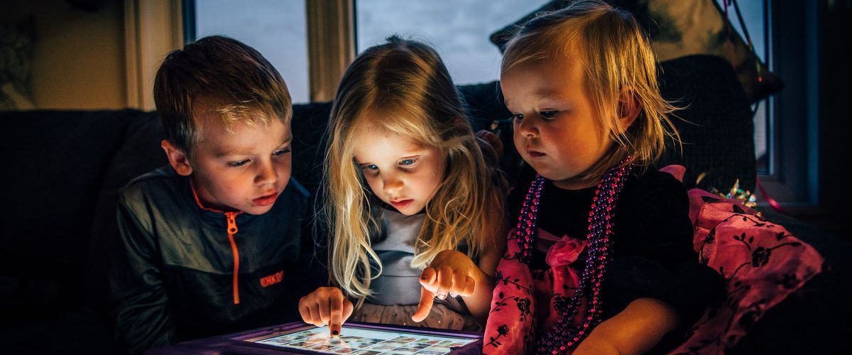 Tre børn i mørket oplyst af en tablet